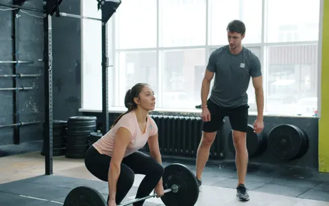 Woman deadlifting a barbell while a personal trainer coaches her in a bright Phuket gym